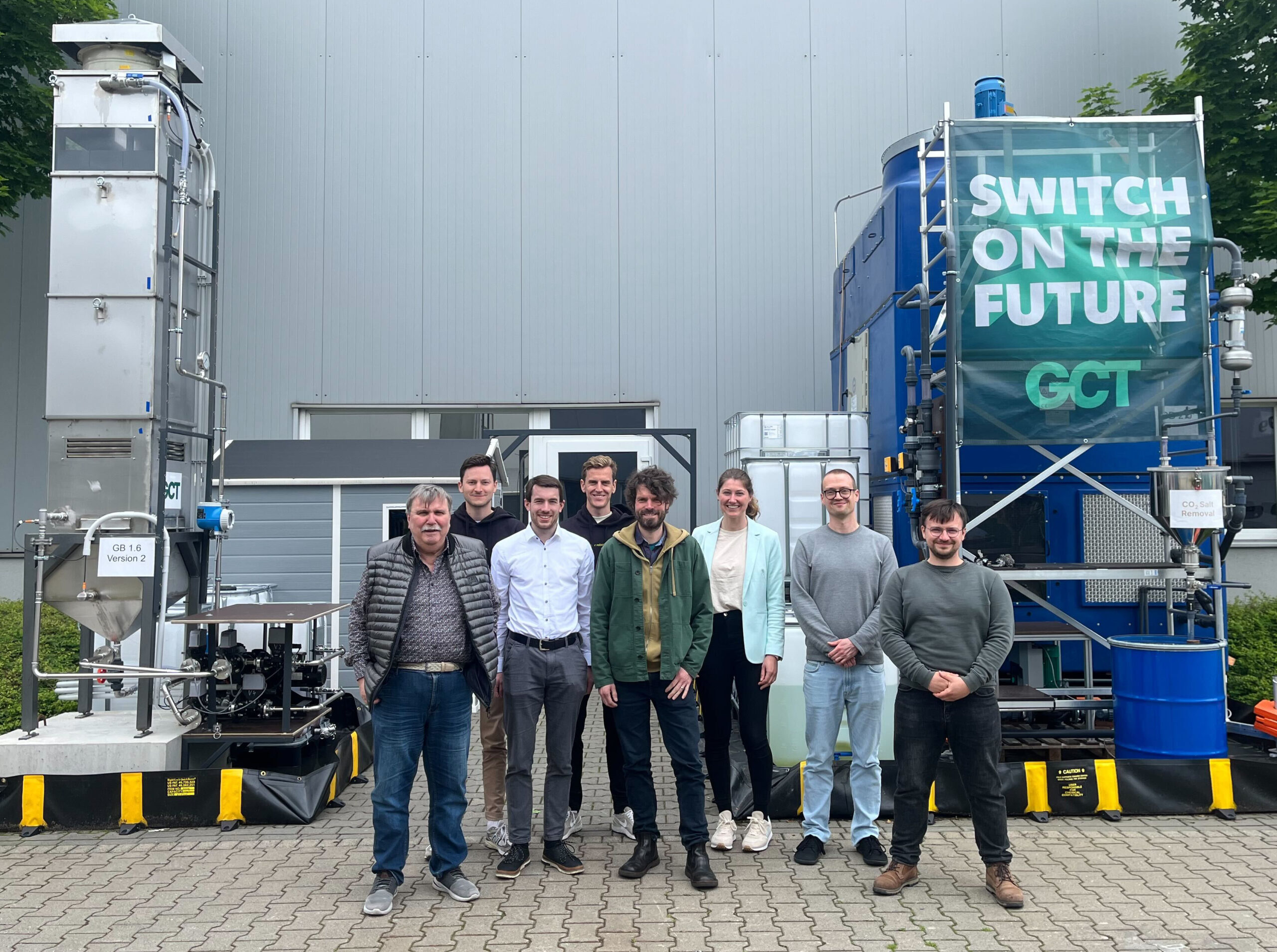 Acht Personen stehen für ein Gruppenbild vor kleineren und großen Maschinen, anlässlich des DAC-2-E-Methane Projektstarts.