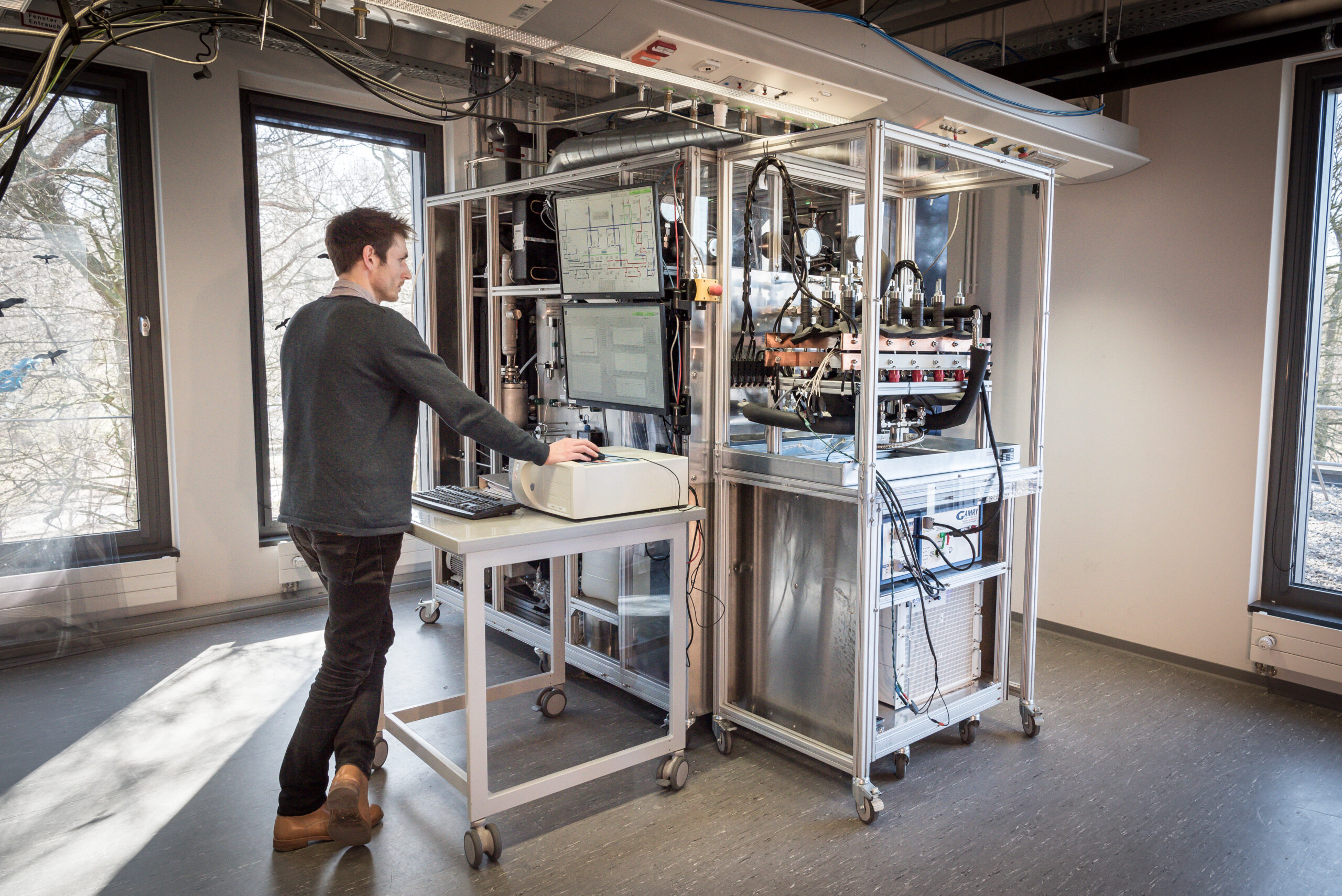 Mann steht an Elektrolyse-Teststand und bedient einen Computer.