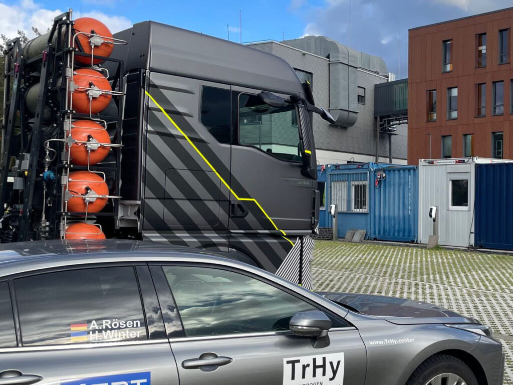 Eine Sattelzugmaschine mit Wasserstofftanks und ein brennstoffzellenbetriebener Pkw stehen während des HeavyDuty Congress 2023 auf dem Parkplatz vor den ZBT-Gebäuden.