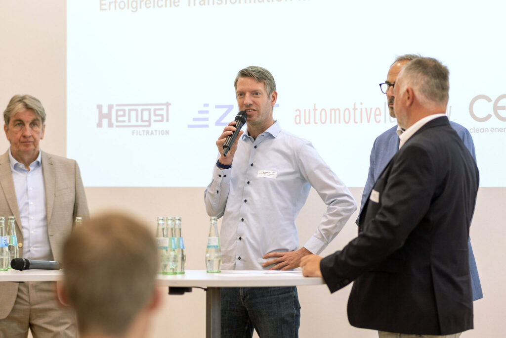 mehrere Personen stehen während eines Vortrag vor einer Leinwand mit Präsentation
