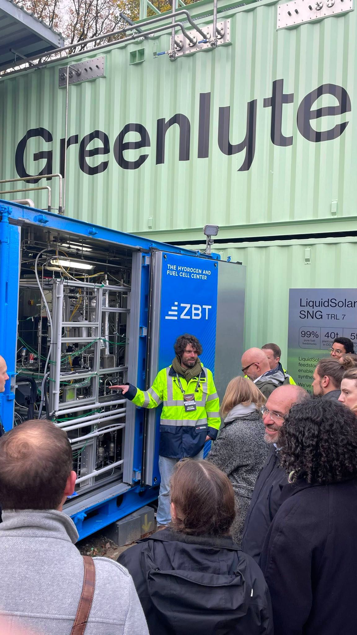 Mann in Arbeitsjacke erklärt einer Menschengruppe die Technologie in einem Überseekontainer