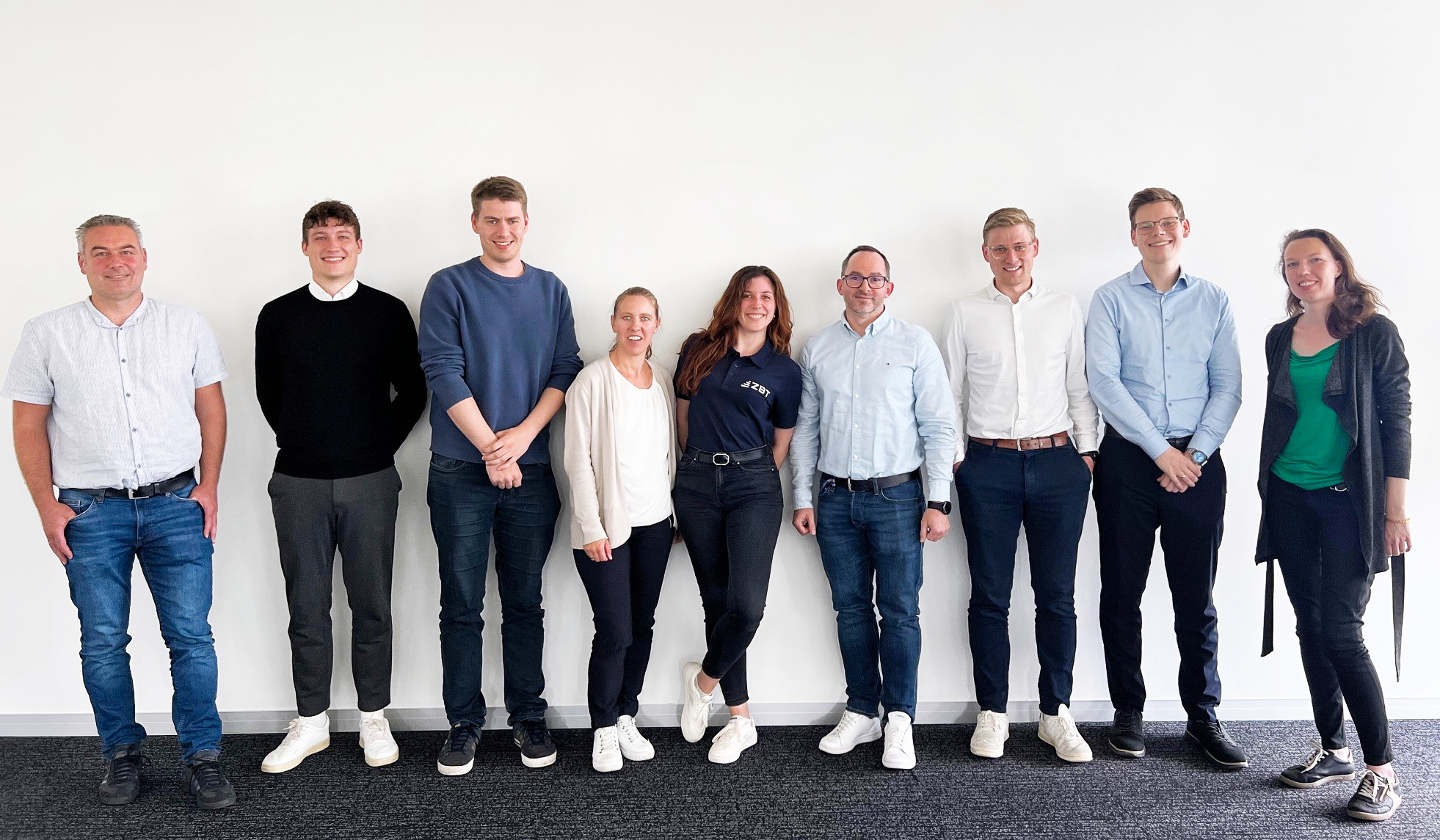 Gruppenfoto von 9 Personen vor einer weißen Wand