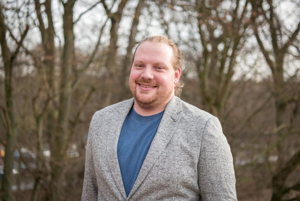 Portrait eines Manns mit Bart und grauem Jacket vor Bäumen